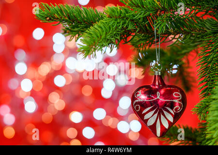 Red Christmas ornament in the form of heart hanging on a fir tree branch on shiny background with copy space for text. Stock Photo