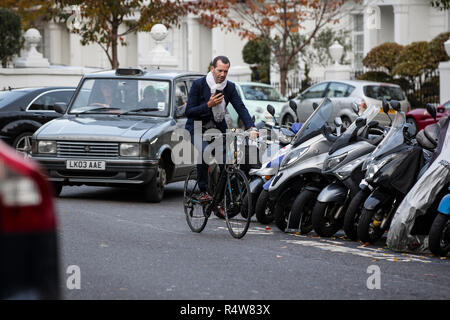 Cyclist on his smartphone whilst cycling in Knightsbridge traffic, London, England, United Kingdom Stock Photo