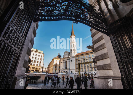 Vienna, Austria - December 24, 2017. St. Michael's Church or Michaelerkirche and Christmas Fair framed with gates. Traditional viennese Xmas market in Stock Photo