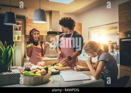 Happy parents and their daughter cooking together in the kitchen while little girl doing her homework on the kitchen table. Stock Photo