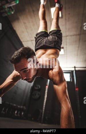 Young muscular man doing hard exercise at the gym. His is doing handstand and whole weight is on his hands. Stock Photo