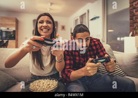 Excited couple is playing video games at home sitting on sofa. They have great weekend in nice company indoors. Stock Photo
