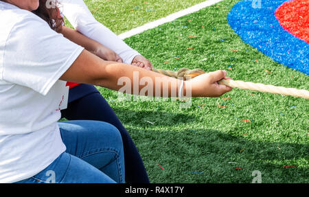 Hands on a rope pulling during a tug of war game on a green turf field. Stock Photo