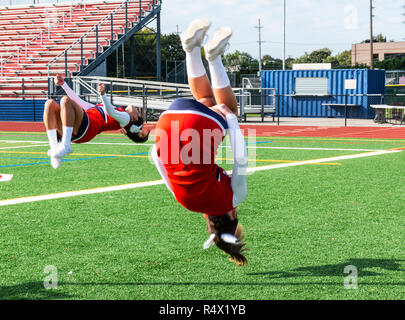 Two high school cheerleaders are practicing flips on the infield before a football game. Stock Photo