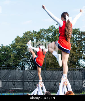 Two high school cheerleading squads holding up their teammates by their ankles while they still perform and cheer. Stock Photo