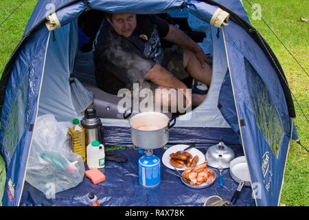 Camping cooking hot food breakfast time in the lake district UK. Biker lifestyle camping trips in small tent. Bacon sausage and eggs for three bikers. Stock Photo