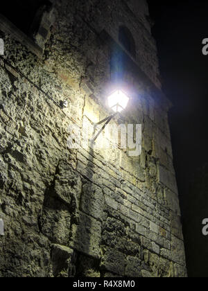 An old wrought iron lamp on a stone wall lighting a dark night in the Gothic Quarter (Barrio Gotico) in Barcelona, Spain Stock Photo