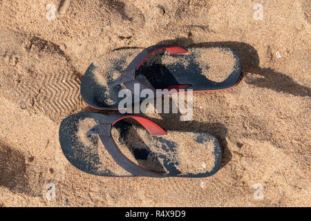 A Close up view of a pair of blue and red slops in the beach sand on a sunny summers day