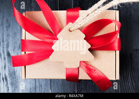 Pine tree label with twine attached on paper present with red ribbon bow. Black natural wooden table. Christmas gift abstract concept. Stock Photo