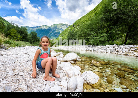 Little girl sitting on river rock after nature hiking. Children resting on rock in mountain river enjoying sunny day. Active family life in nature. Be Stock Photo