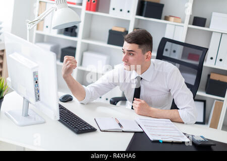 A young man sitting at a computer Desk in the office and shows his fist in the monitor. Stock Photo