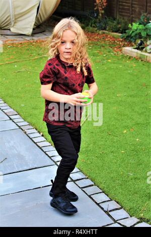 A young, Caucasian, long haired boy plays with a ball in a garden Stock Photo