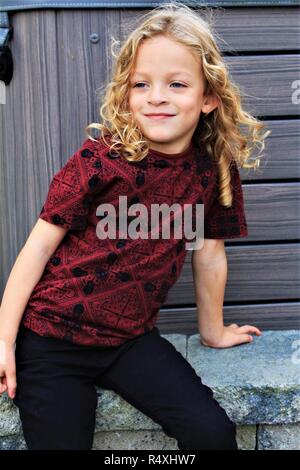 A young, Caucasian, long haired boy sat posing like a model. Stock Photo