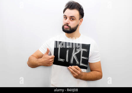 Young man stand and hold plate with work like. He points on it. Young man looks at camera. He is serious. Isolated on white background. Stock Photo