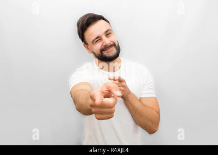 Very positive young man points on camera and whinkles to it. He smiles. Isolated on white background. Stock Photo