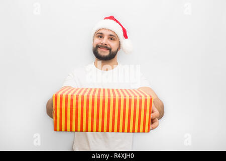 Positive and nice young man in red hat holding orange striped bow with present in both hands. He looks confident. Isolated on white background. Stock Photo