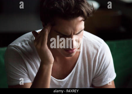 Young man sitting on couch at home have a headache Stock Photo