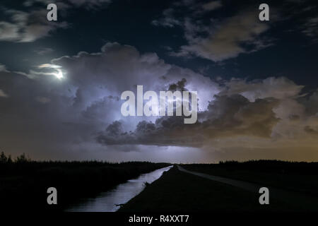 Thunderstorm clouds are illuminated by lightning. The moon is partly obscured by the storm. Location: close to the cities of Gouda and Leiden, Holland Stock Photo