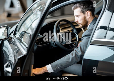 Portrait of a handsome businessman sitting on the driver seat of a luxury car in the showroom Stock Photo