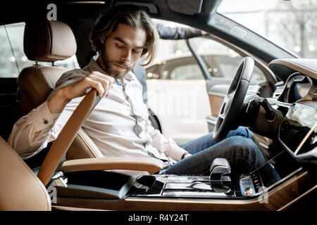 Young handsome man trying a new car sitting in the luxury car interior at the showroom Stock Photo