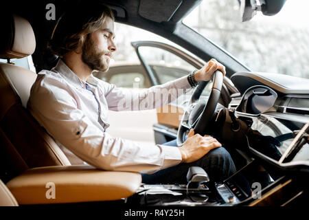 Young handsome man trying a new car sitting in the luxury car interior at the showroom Stock Photo