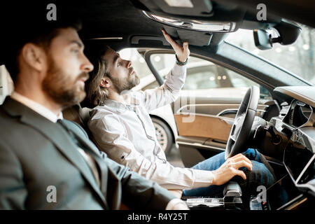 Young man trying new car sitting with salesperson in the luxury car interior at the showroom Stock Photo