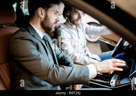 Young man trying new car sitting with salesperson in the luxury car interior at the showroom Stock Photo