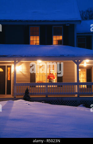 Young woman looks out of cozy suburban home window onto freshly fallen snowfall, Northeast, USA Stock Photo