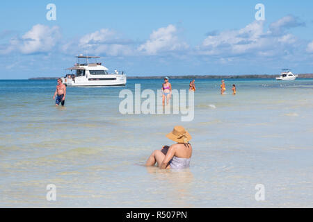 Woman wearing a straw hat sits in the clear blue waters of the Caribbean on a beach in Cuba. Stock Photo