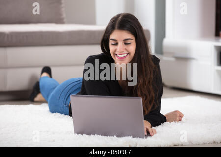 Young Woman Lying On Rug Using Laptop Stock Photo