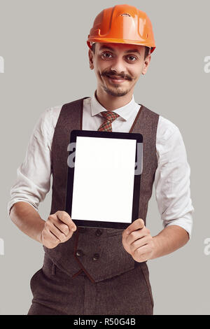 Portrait of handsome young confident arabic architect with fancy mustache in woolen suit and construction helmet holds tablet Stock Photo