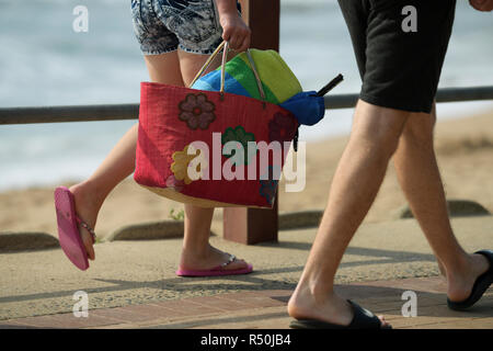 Durban, KwaZulu-Natal, South Africa, legs of young woman carrying colourful red beach bag walking with male companion on seaside promenade, beach Stock Photo