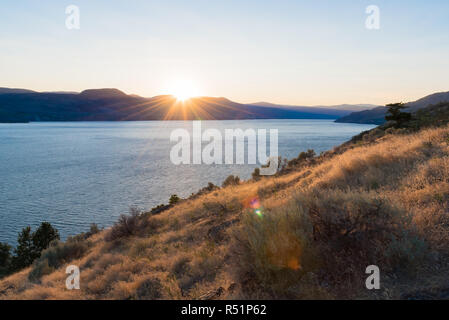 Sun setting behind the mountains over Okanagan Lake in summer Stock Photo