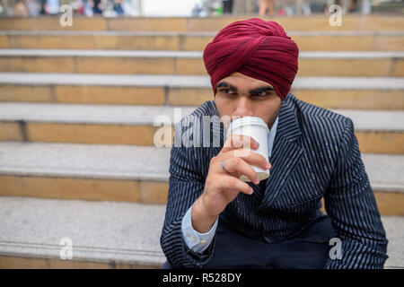 Indian businessman sitting outdoors in city while drinking coffee Stock Photo