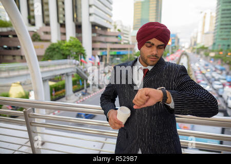 Businessman outdoors in city checking time from watch and holding coffee cup Stock Photo