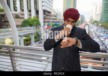 Businessman outdoors in city checking time from watch and drinking coffee Stock Photo