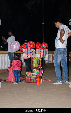 A very young girl child selling balloons on the footpath during the 49th International Film Festival of India in Panaji, Goa, India. Stock Photo