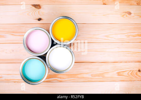 Four open cans of paint on wooden natural background. Yellow, white, pink, turquoise colors. Top view. Stock Photo