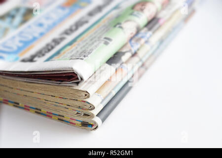 Stack of newspapers and magazines with colorful pages (headlines, articles), latest news in daily papers. Tabloid journals stacked in pile on white Stock Photo