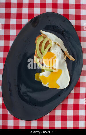 Avocado toast with fried egg . Sliced avocado and egg on toasted bread on black dish  for healthy breakfast or snack on table , copy space. Stock Photo