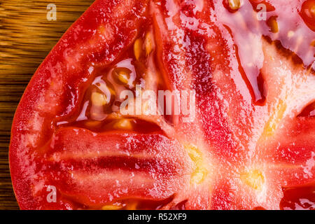 A Macro image of a single tomato slice on a bamboo cutting board.  Focus is very sharp and colors vivid and realistic. Stock Photo