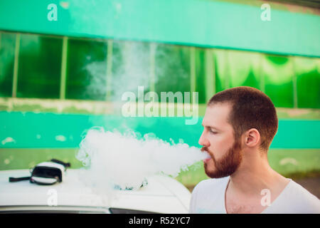 Man vaping e-cigarette with e-liquid, close-up, breathes out large cloud of steam or vapor. Vape concept Stock Photo
