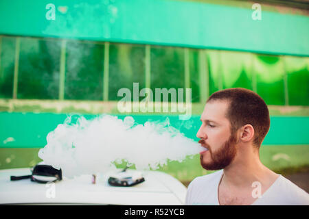 Man vaping e-cigarette with e-liquid, close-up, breathes out large cloud of steam or vapor. Vape concept Stock Photo