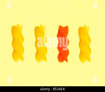 Four multicolor raw fusilli pasta in a row isolated on light yellow background. Top view. Abstract food background Stock Photo