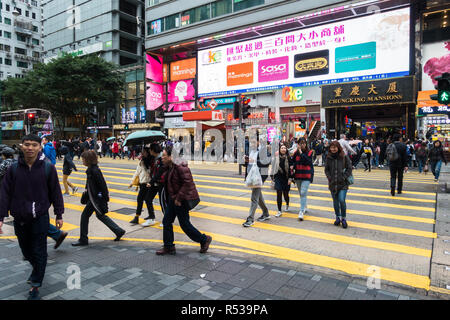 People walking across Nathan Road with Chungking Mansions entrance in the background, a famous complex building with cheap hotels and shops, Hong Kong Stock Photo