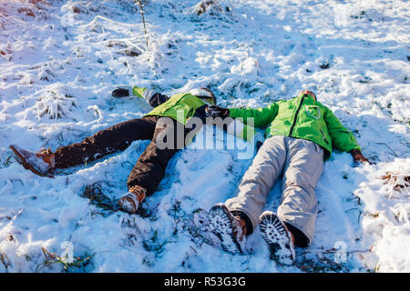 Young couple in love lying in snow and making snow angels. Happy people having fun in winter forest. Seasonal activities Stock Photo
