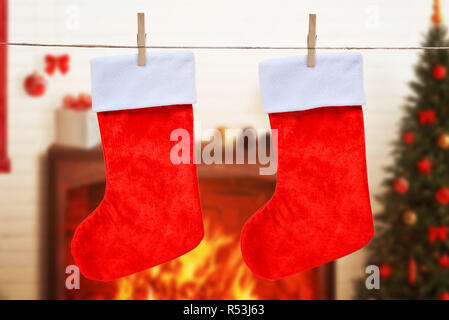 Christmas empty red socks hung on the rope. Fireplace, decorations and tree in background. Stock Photo