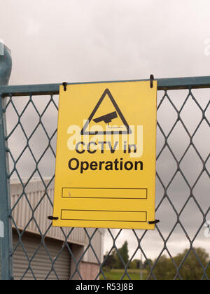 yellow sign on fence saying cctv in operation Stock Photo