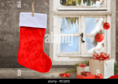 Empty Christmas sock hanging on a rope. Clean sock for mockup, greeting text. Christmas gifts, balls, decorations and window in background. Stock Photo