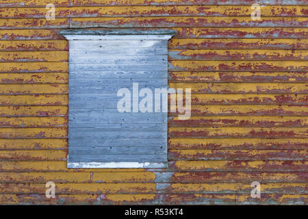 Closed window of old wooden shed with decayed yellow and red paint Stock Photo